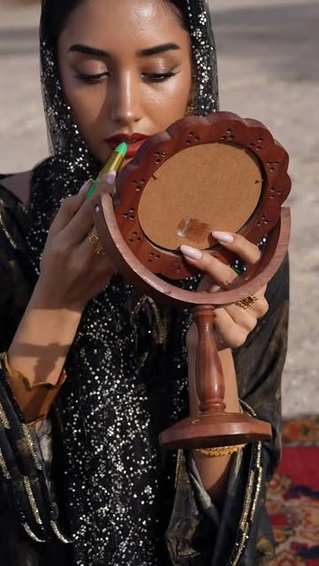 Model holding a hand mirror in a beaded abaya